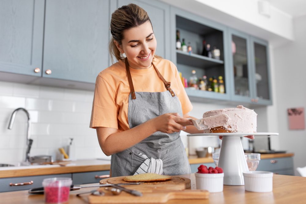 A smiling woman puts the icing on a cake.