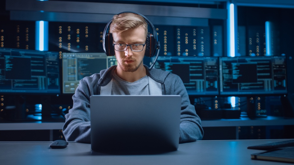 A man in a headset focuses on the output of a laptop.