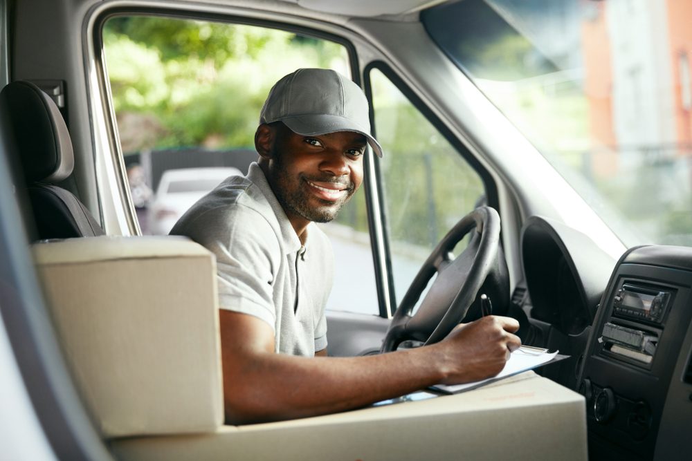 A man in the driver's seat of a bix truck writes on a clipboard.