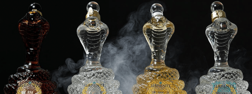 Four serpent-shaped bottles of Serpiente tequila sit against a black background with smoke.