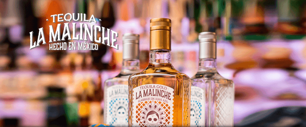 Three bottles of Tequila La Malinche are placed in front of a bar.