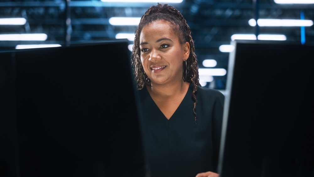 A woman hosting game servers smiles at two screens. 