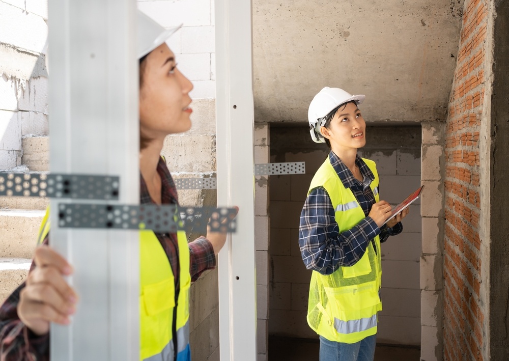 Two women inspect the wall of a brick house.