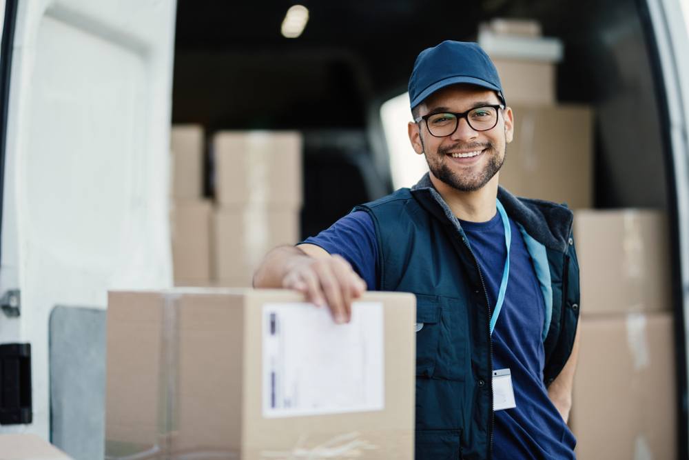 A smiling man in glasses leans against a stack of boxes.