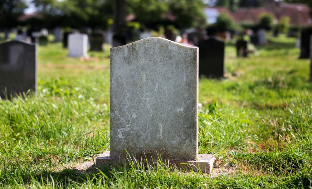 blank gravestone sitting in graveyard with overgrown grass