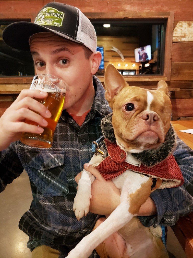 man drinking beer in trucker hat with boston terrier dog.