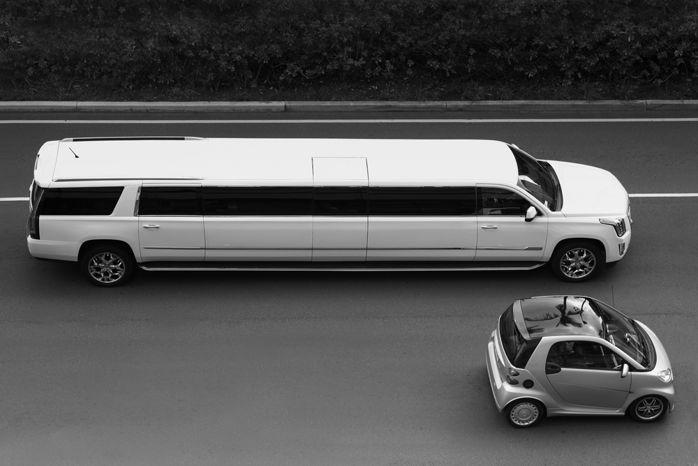 black and white photo of super stretch limousine and small electric car to demonstrate 