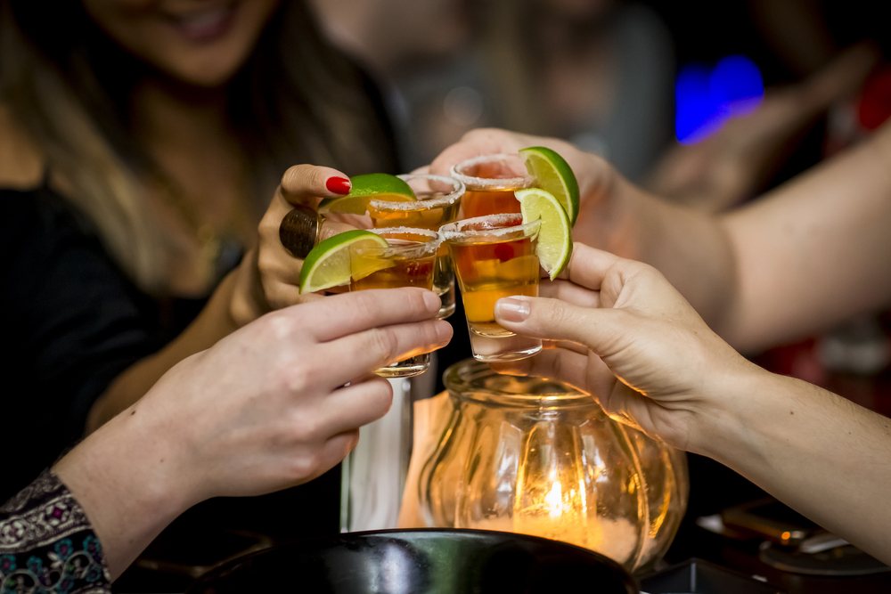 Four hands toast with glasses of tequila.