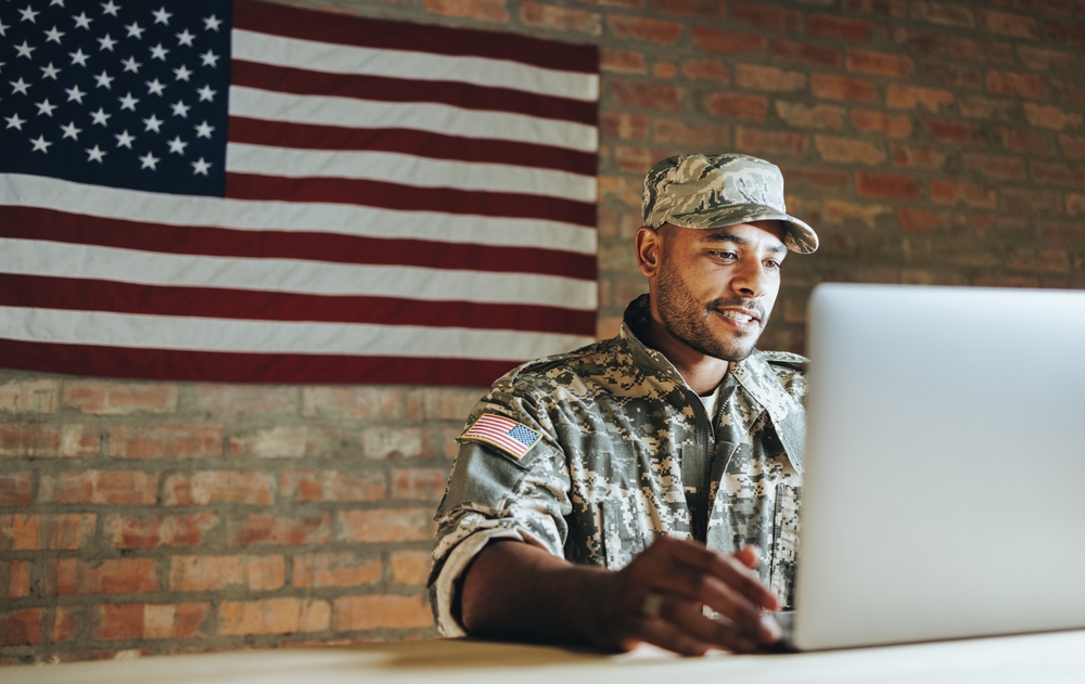 military veteran on laptop running digital clothing company with bricks and american flag in background