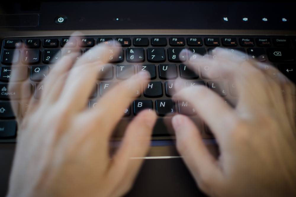 blurred fingers typing fast on laptop keyboard