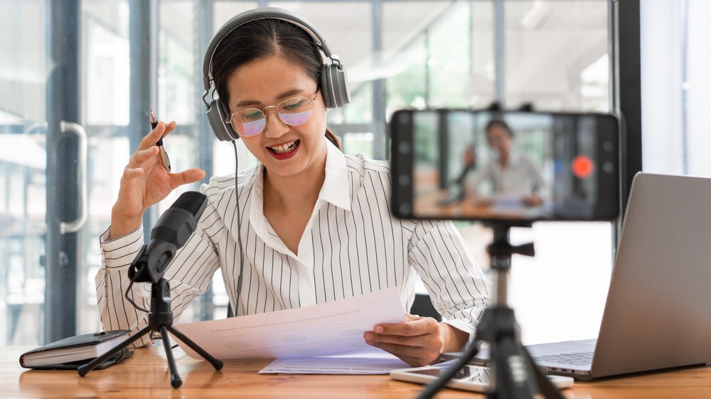 A woman in a headset reads a script and talks into a microphone.