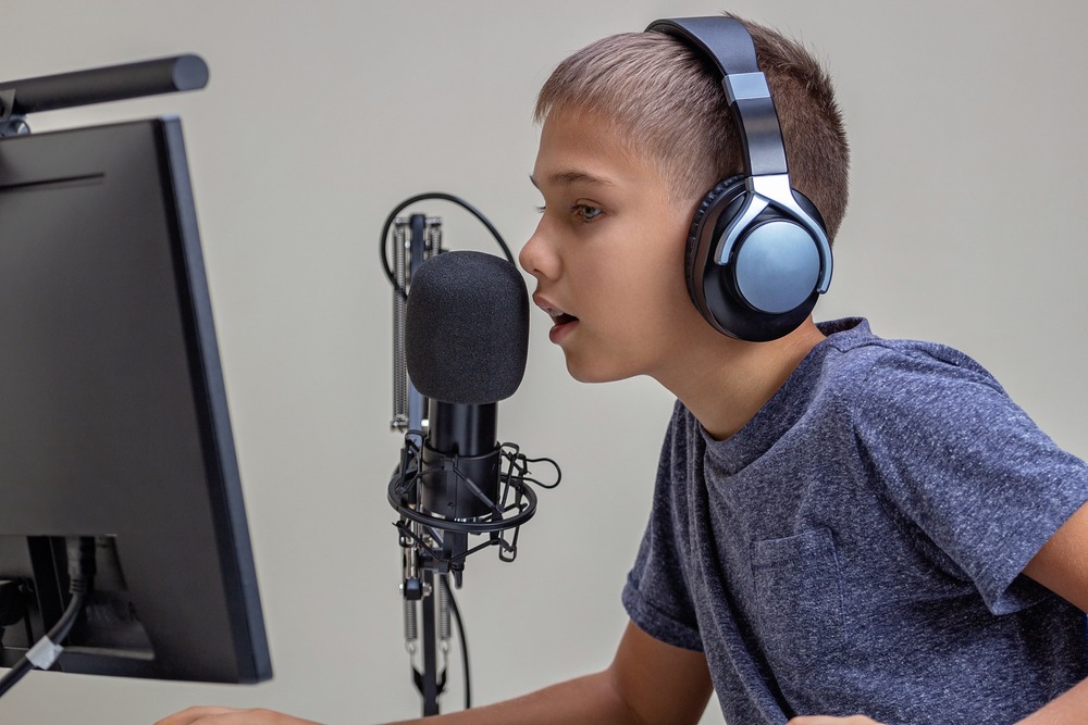 A boy talks into a mic while recording a podcast on his computer.