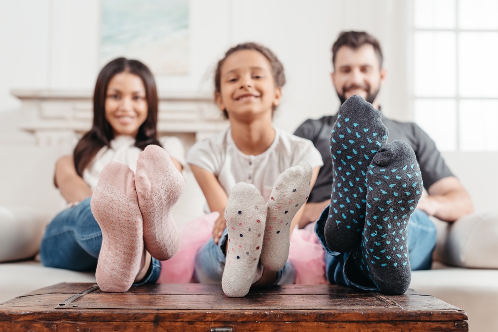 A man, woman, and child show off their new socks with their feet on the table.