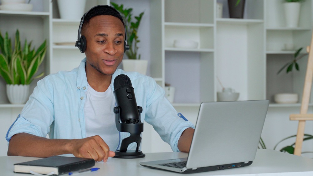 A man talks into a large black microphone while typing on a silver computer.