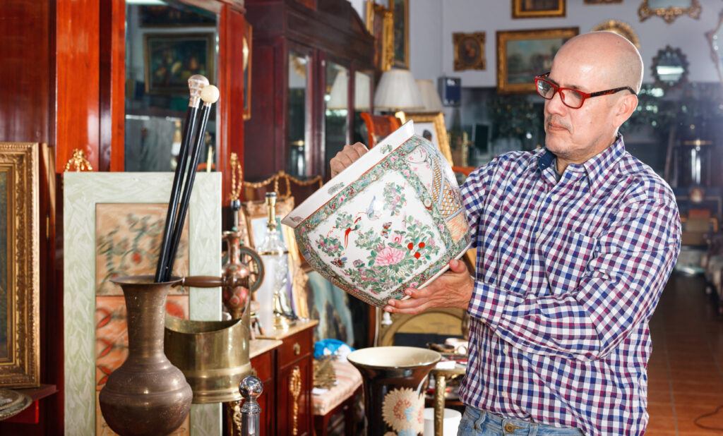 Man with glasses examining an antique vase in a store