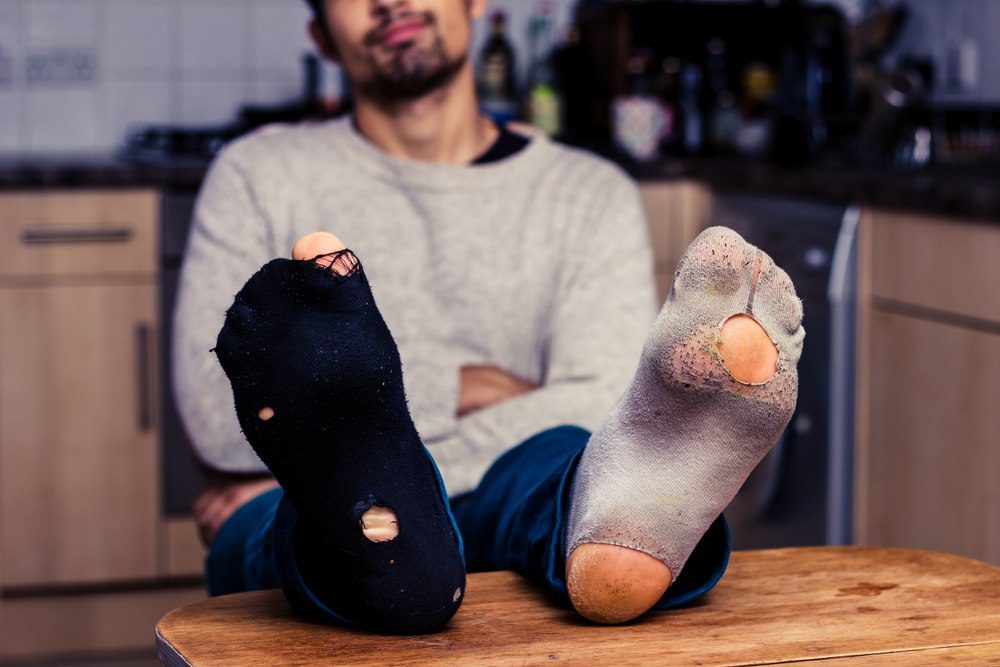 A man wears mismatched socks with holes. 