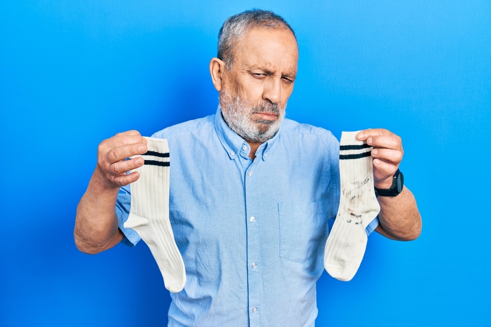 A man holds up a pair of socks with a questioning look.