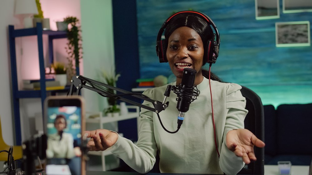 A woman in headphones holds her hands out while she talks into a mike. 