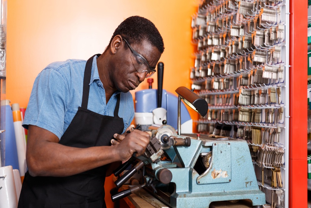 professional locksmith working with keys on a vice grip on workshop table with many types of keys in the background