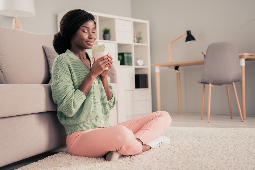 african american woman drinking a cup of tea on the living room floor