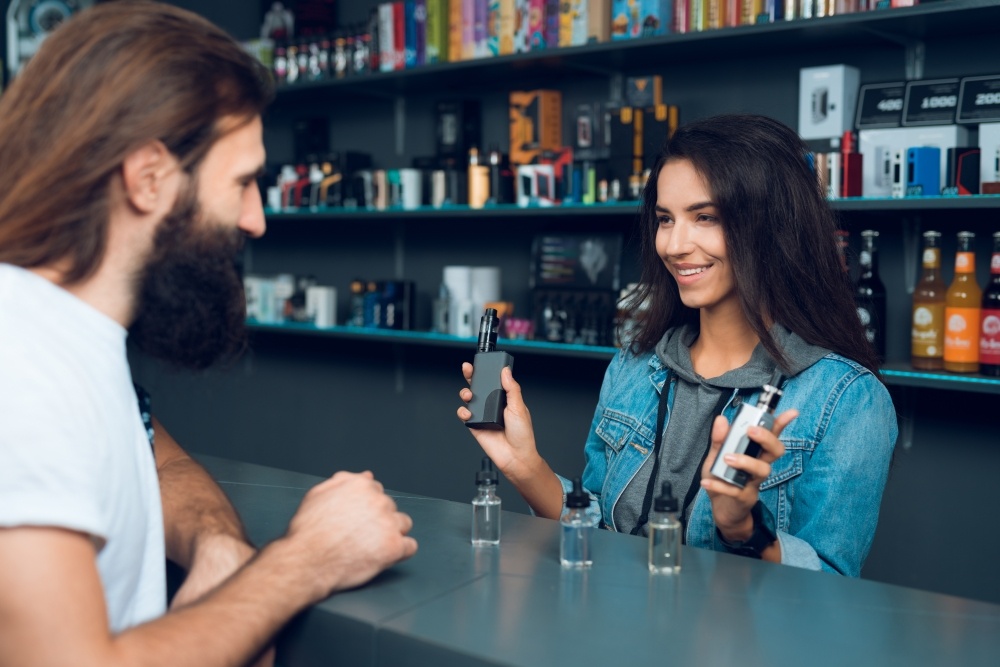 woman working at smoke shop showing man with beard a variety of products to purchase